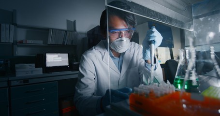 Portrait of Chinese male scientist is analyzing with a pipette a liquid to extract the DNA and molecules in the test tubes in laboratory. 