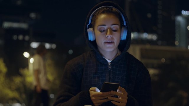 Beautiful Female Listening To Music on Wireless Headphones dancing During Training In city skate Park wearing a sweatshirt hoodie