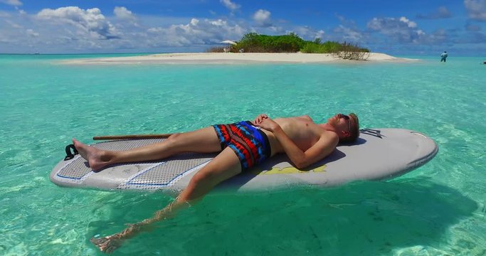 A young man relaxing and resting in his surf board away from the beautiful island in the middle of the shallow ocean beneath the blue sky in Philippines - normal shot