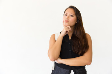 Fototapeta premium Thoughtful woman with backpack looking at camera. Portrait of beautiful pensive young woman with backpack standing with hand on chin and looking at camera on white. Facial expression concept