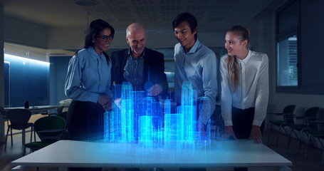 A group of modern designers are using a futuristic sophisticated technology screen with augmented reality holograms for a new project realization in an office.
