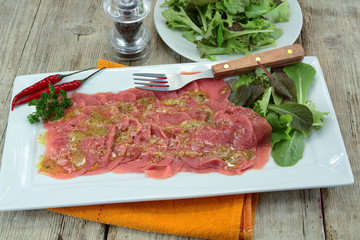 beef carpaccio on a plate, accompanied by salad
