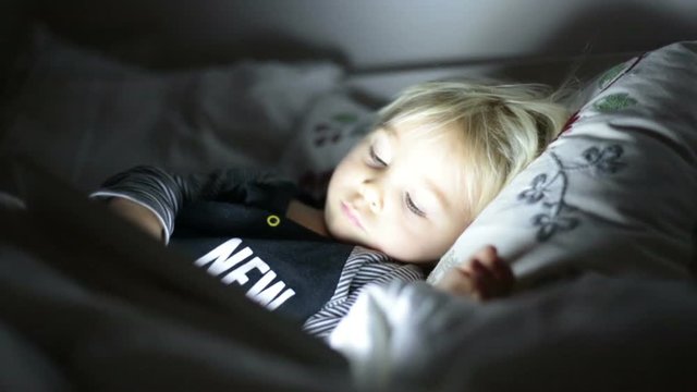 Happy toddler boy watching nights story tale at night on tablet in ebd