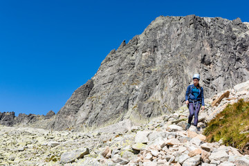 Mountaineer in a helmet going down the path in the mountains. In the background there is a visible wall which climbing routes lead to the popular peak (Baranie rohy, Baranie Rogi). Tatras, Slovakia.