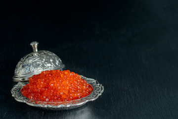 Red caviar in silver bowl on black background