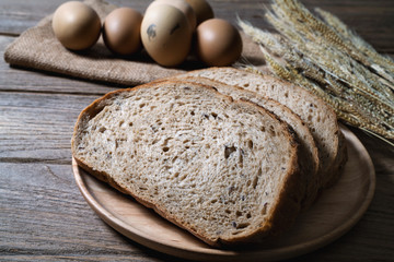 bread loaf and wheat ears and eggs on wooden background.