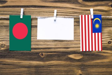 Hanging flags of Bangladesh and Malaysia attached to rope with clothes pins with copy space on white note paper on wooden background.Diplomatic relations between countries.