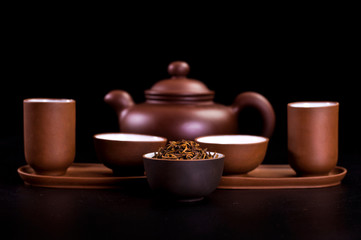 Obraz na płótnie Canvas Asian tea ceremony. Clay teapot and tea cups with dry tea leaves on a black background.