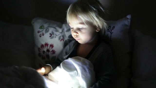 Happy toddler boy watching nights story tale at night on tablet in ebd