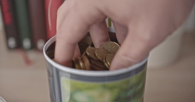 Male hand takes a handful of euro coins and bank note from a jar