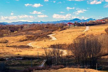 winding road thru hills in early spring time and snow covered mountain peaks in the far background