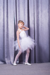 Naklejka premium Little cute girl in a white dress on the background of theatrical curtains.