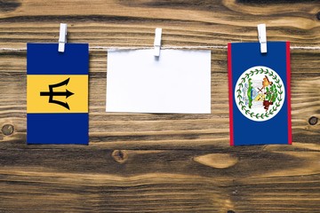 Hanging flags of Barbados and Belize attached to rope with clothes pins with copy space on white note paper on wooden background.Diplomatic relations between countries.