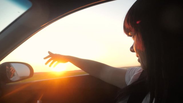 road travel trip concept. girl waving her hand in the window sunlight the wind In car slow motion video. brunette girl put her hand out the window sunlight sunset lifestyle