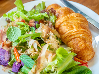 Croissant with vegetables salad in white dish on wooden table for breakfast