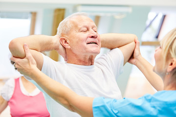 Therapeutin hilft Senior Mann beim Rückentraining