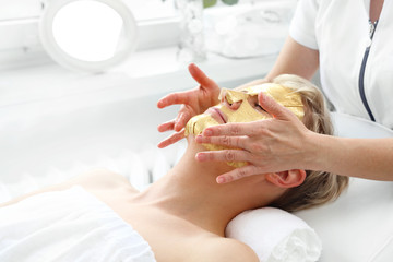 Obraz na płótnie Canvas Gold mask on the fabric, Anti-wrinkle mask. Woman in a beauty salon. The beautician applies a golden mask to a woman's face. Beautiful woman in a beauty salon during facial treatment