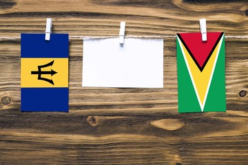 Hanging flags of Barbados and Guyana attached to rope with clothes pins with copy space on white note paper on wooden background.Diplomatic relations between countries.