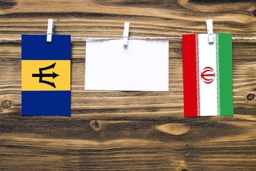 Hanging flags of Barbados and Iran attached to rope with clothes pins with copy space on white note paper on wooden background.Diplomatic relations between countries.