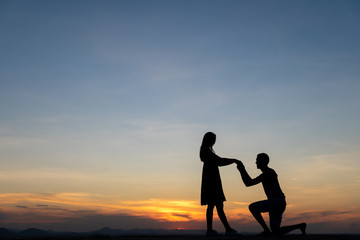 Fototapeta na wymiar Silhouette couple man down on one knee proposing to woman under sunset sky background
