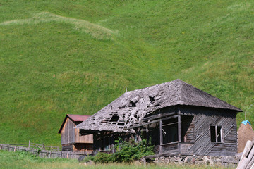 Fototapeta na wymiar old abandoned wooden house with green grass hills in the background