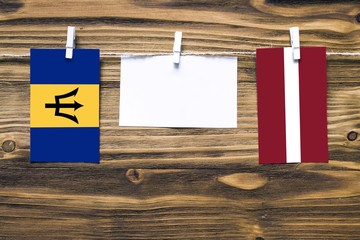 Hanging flags of Barbados and Latvia attached to rope with clothes pins with copy space on white note paper on wooden background.Diplomatic relations between countries.