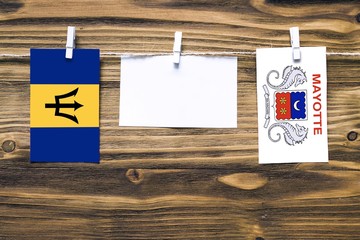 Hanging flags of Barbados and Mayotte attached to rope with clothes pins with copy space on white note paper on wooden background.Diplomatic relations between countries.