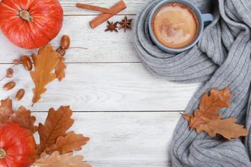 Grey mug of coffee wrapped in plaid or scarf, spices, dry oak leaves, acorns, orange pumpkins on white wooden table. Autumn drink concept. Fall, pumpkin spicy latte, thanksgiving, top, copy space