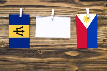 Hanging flags of Barbados and Philippines attached to rope with clothes pins with copy space on white note paper on wooden background.Diplomatic relations between countries.