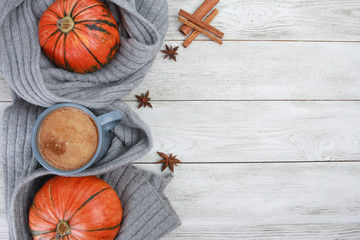 Grey cup of coffee wrapped in plaid or scarf, orange pumpkins, spices, anise, cinnamon on white wooden table. Autumn drink concept. Fall, pumpkin spicy latte, thanksgiving, top, copy space