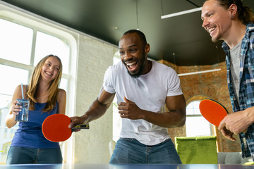 Young people playing table tennis in workplace, having fun. Friends in casual clothes play ping...
