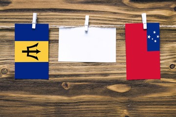 Hanging flags of Barbados and Samoa attached to rope with clothes pins with copy space on white note paper on wooden background.Diplomatic relations between countries.