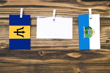 Hanging flags of Barbados and San Marino attached to rope with clothes pins with copy space on...