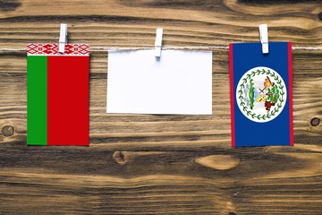 Hanging flags of Belarus and Belize attached to rope with clothes pins with copy space on white note paper on wooden background.Diplomatic relations between countries.