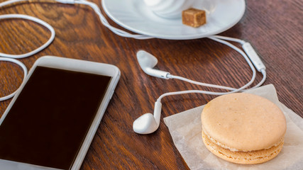 Business concept: Phone with headphones, a cup of coffee and a cake on the table. Close-up