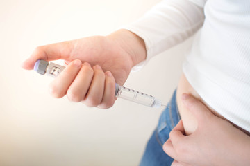 Close up of female diabetes patient making subcutaneous insulin injection into her abdomen with insulin pen syringe for at home. Diabetes, health care and medical concept. Diabetes World Day.