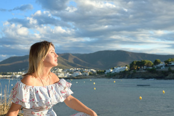 Woman sitting in front of a coastal landscape of the northern mediterranean on a summer afternoon with wind taking a sunbath with copy space