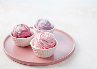 Three types of meringue on a pink plate. The taste of strawberries, lavender and blackcurrant