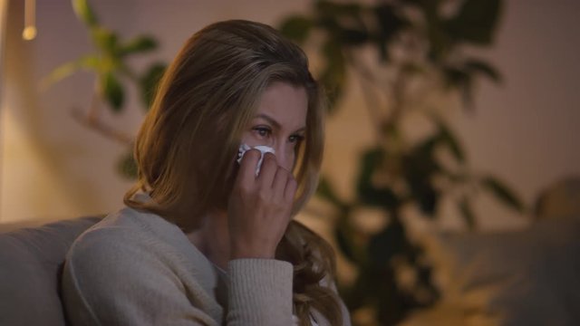 Tracking of sad woman sitting on couch and crying while watching drama on TV in evening