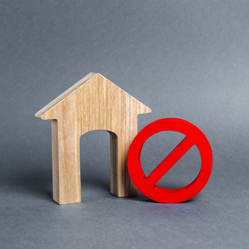 Wooden house figurine and a red prohibition symbol NO. Concept of inaccessibility or lack of housing. There is no opportunity to buy a house or pay for rent. The house can not be put into operation.