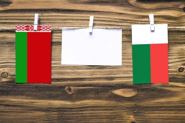 Hanging flags of Belarus and Madagascar attached to rope with clothes pins with copy space on white note paper on wooden background.Diplomatic relations between countries.