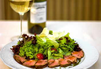 cold cuts Parmesan cheese salad on a white plate, a glass of white wine, a delicious and satisfying snack