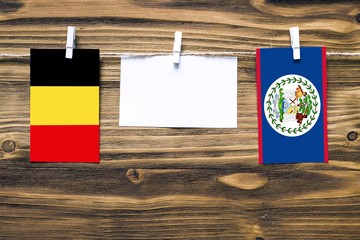 Hanging flags of Belgium and Belize attached to rope with clothes pins with copy space on white note paper on wooden background.Diplomatic relations between countries.