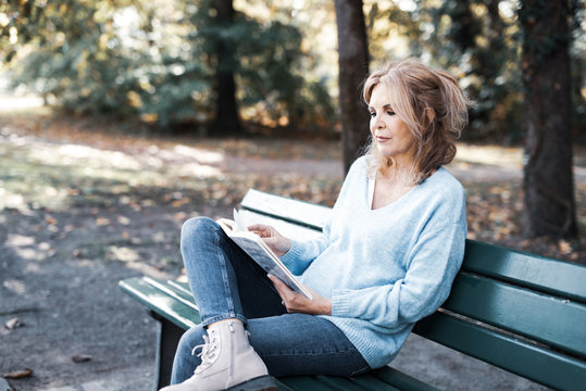 Frau im mittleren Alter sitzt lesend auf einer Bank