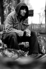 Homeless, sad man in a beanie sitting outside and feeling cold, trying to warm up his hands