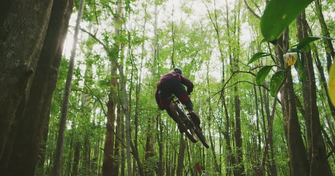 Extreme sports mountain bikers catch big air in slow motion, two friends mountain biking together in a green forest, fun outdoors summer activities