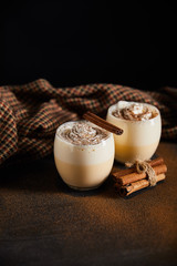 eggnog cocktail with whipped cream, cinnamon sticks and checkered cloth on table covered with cinnamon powder isolated on black