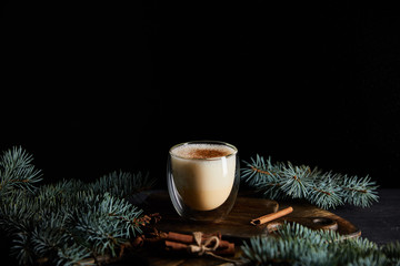 delicious eggnog cocktail on cutting board near spruce branches and cinnamon sticks isolated on black