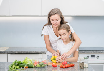 Happy family - mother and young girl preparing vegetarian salad at home in kitchen