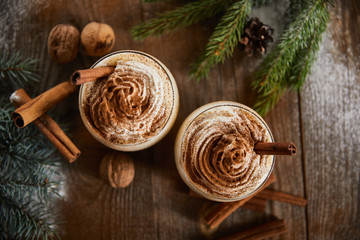 top view of delicious eggnog drink near spruce branches, wallnuts and cinnamon sticks on wooden table